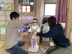 保健師に身長を測ってもらう幼児と、幼児の頭を固定する父