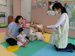 しゃぼん玉を歌いながら出し物をする先生と見つめる親子