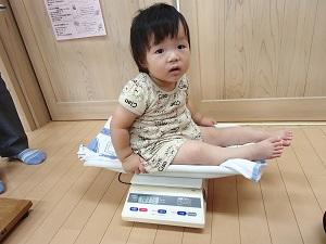 ベビー用体重計にカメラ目線で座って計測している赤ちゃんの写真