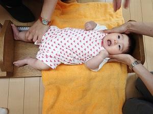 頭と足を真っ直ぐになるように伸ばされ、乳児用ベッド型身長計に寝かされ計測されている赤ちゃんの写真