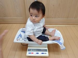 ベビー用体重計に左後ろを見ながら座って計測している赤ちゃんの写真