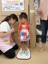保健師さんの方を見ながら身長計に立っている女の子と身長測定をしてる保健師さんの写真