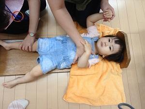 足を伸ばされ泣き出しそうな顔をして乳児用ベッド型身長計に寝かされている子どもの写真