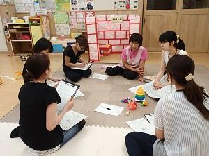 円を描くように丸くなって座って資料を見ながら話をしている母親と保育士、栄養士の写真