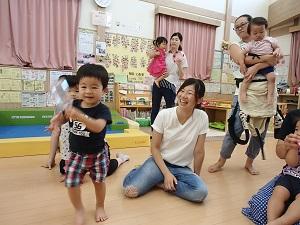 笑顔の母親の左前で黒色のシャツを着た男の子が、左手でペットボトルを持ち走っている写真