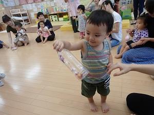 参加者の親子が円になって座っているなか、ボーダー柄のタンクトップを着た男の子が、右手でペットボトルを持って見ている写真