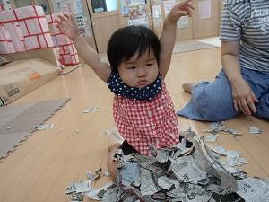 チェック柄のシャツを着た子供が、座っている膝の上にビリビリに破いた新聞紙を乗せ両手を上げている写真