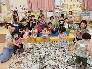 子供の遊びスペースの前にビリビリに破いた新聞紙を広げ、後ろで参加した親子が集まって座っている集合写真