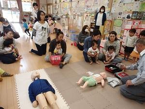 乳児のAEDの使用方法について人形を使いながらレクチャーする太田救急救命士とそれを聞く参加者たちの写真