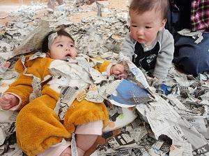 たくさんの破られた新聞紙に埋もれている2名の赤ちゃんの写真