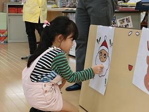 サンタクロースのイラストに口のパーツをつけている女の子の写真