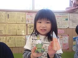 紙で出来た三角形の人形を両手に持っている女の子の写真