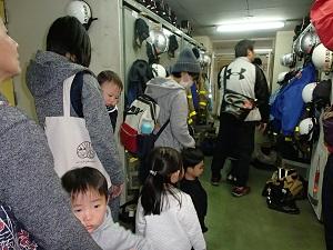 庁舎内のヘルメットが設置されたロッカーを見学するお父さん、お母さん、子供達の写真