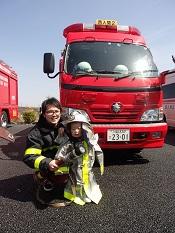 消防車の前に防火服装着を着た親子が記念写真