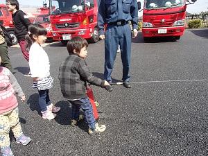 後ろには消防車が並び、男の子が消火器を使い消火訓練体験する写真