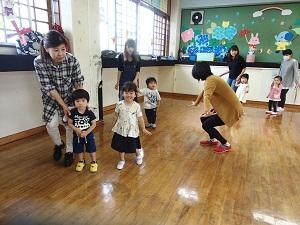 先生が膝をまげてポーズを決めている周りで、円を囲むように列になってレクレーションをしている写真
