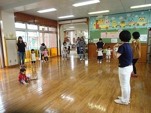 前で先生が両手を肩に置くポーズを、周りの親子たちが先生の真似をしている写真