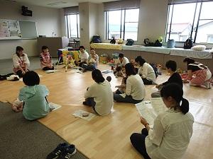 子育て支援室内にて、床に円状に集まって座り助産師さんの話を聞く参加者達の写真