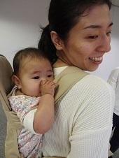 お母さんにおんぶされた赤ちゃんが、お母さんの背中で指しゃぶりをしている写真