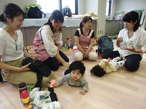 赤と白のチェックのエプロンをつけた助産師2名と赤ちゃんをあやしながら談笑する2名の母親の写真
