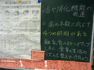 黒板に張り出された離乳食の進め方目安まとめの紙と手書きの補足説明文が映し出された写真