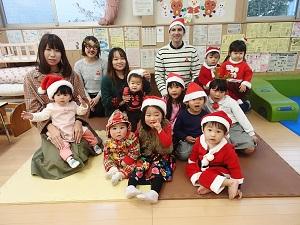 サンタクロースの衣装を着た子どもやサンタクロースの赤い帽子を被った子ども達と保護者、外国人の先生が集まって写っている集合写真