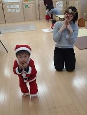 サンタクロースの赤い衣装を着た男の子が両手人差し指を口元の持っていくポース、後ろにトナカイの眼鏡をかけた女性が両手の人差し指を顎の下の持っていき斜め上を見るポースをしている写真
