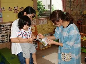 母親に抱っこされた子供が、女性の先生からスタンプをもらっている写真