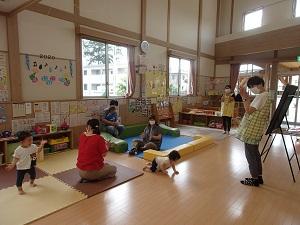 手拍子をしている二人の職員と自由に遊んでいる子供たち、子供たちを見守る保護者の写真