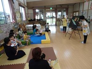 皆の前に立ち、黒板に天の川のイラストを貼り付ける職員と、それを座って見ている子供と保護者たちの写真