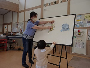 パネルシアターをする先生とパネルに手を伸ばす男児
