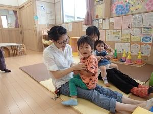 膝の上に乗っている子供たちの両手を取る母親たちの写真