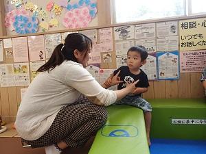 緑色のブロックの上に座る子供と子供に手を掴まれている母親の写真