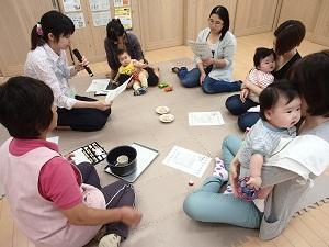 マイクを持って資料を見ながら話をしている栄養士と資料を見ながら話を聞いている母親と保育士の写真