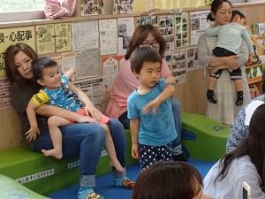 お母さんに抱っこされて笑顔で座っている子ども達と前方をじっと見ている男の子の写真