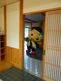 公民館の玄関で待機しているゆるキャラ「もろ丸くん」が両手を広げて頭を左に傾けている写真