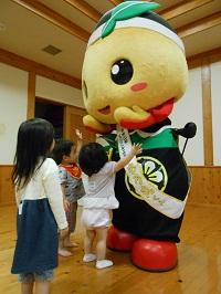 2名の子どもが、ゆるキャラ「もろ丸くん」に触り、女の子が離れた所で見ている写真