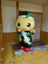公民館の玄関から入ってきた、ゆるキャラ「もろ丸くん」が両手を平行にして歩いている写真
