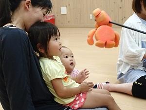 人形を母親の膝に座る子供たちの前に見せている様子の写真
