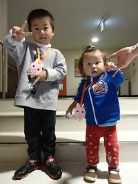 ピースサインをしている男の子と、その横で、大人の手を握りながら立っている子供の写真