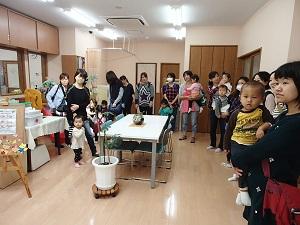 中央に机と椅子が設置されている室内に親子連れの参加者がずらりと並んでいる写真