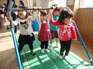 マットの上に置かれた鉄棒に手を伸ばしている4人の女の子の写真
