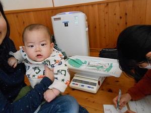母親に抱かれている赤ちゃんと記録用紙に書き込んでいる保健師の写真