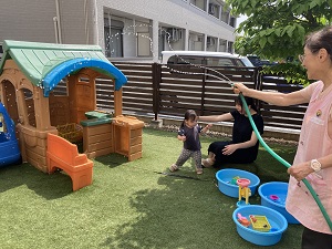 水をまく先生と水遊びをする親子