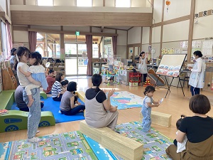 はたらく車のペープサートをする先生と、それを見る親子たち