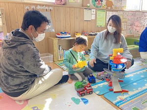 車で遊ぶ幼児と見守る両親