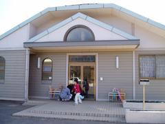 グレーで入り口屋根が三角で真ん中に半円のガラス窓がある光山学童保育所の入り口から全体を写した写真