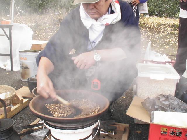 素焼きの土器皿の上で煙をたてながら穀物を混ぜている男性の写真