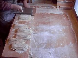 麵打ち台の上で、麵切り包丁を使い、うどん生地をたくさん切っている様子の写真