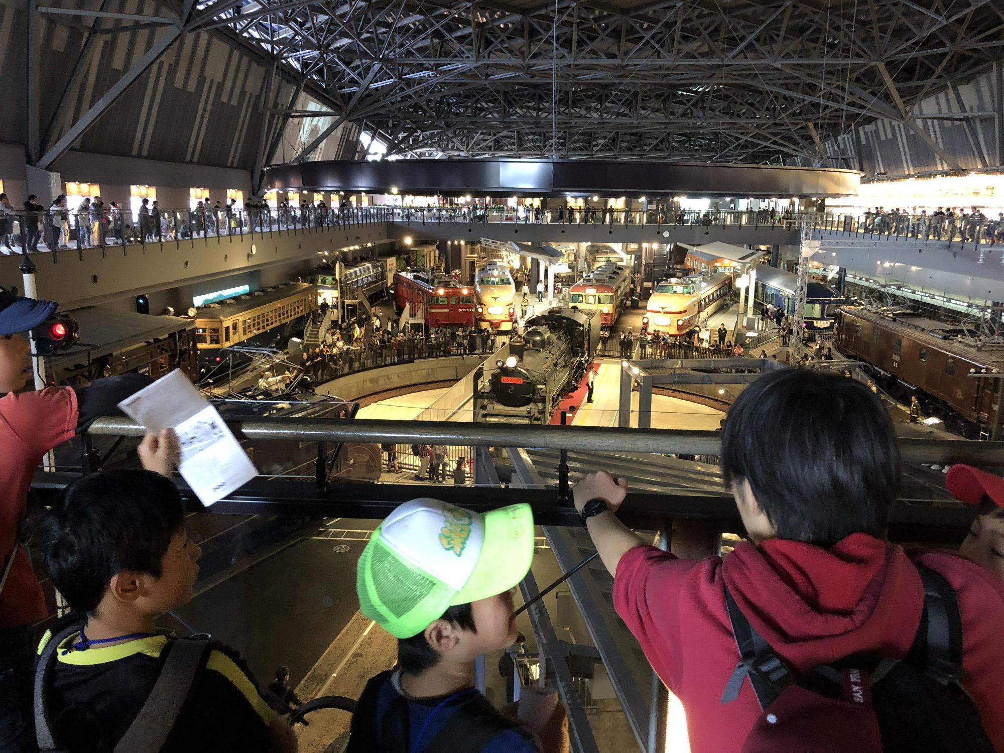 階下に展示されている蒸気機関車を、2階の観覧スペースで話している女性の話しを子供たちが聞いている写真
